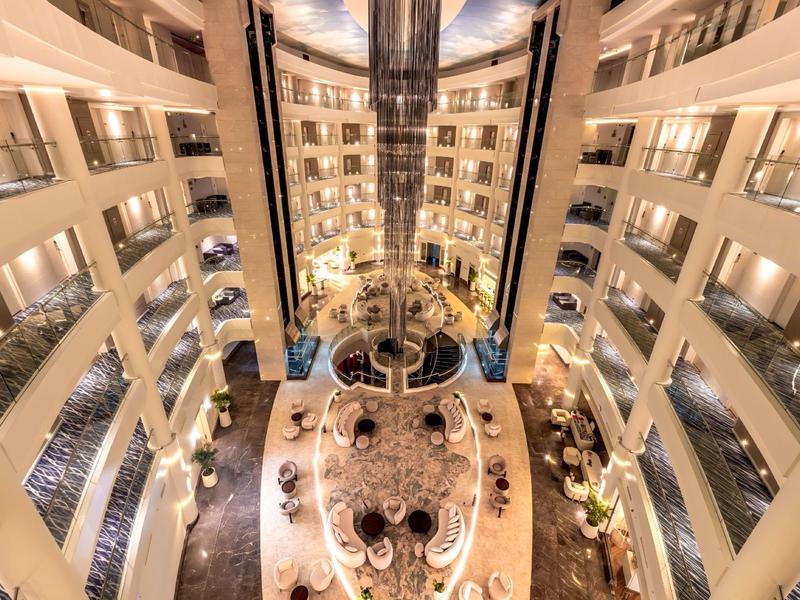 Atrium d'hôtel luxueux avec plusieurs étages, ascenseurs et décorations sous un éclairage chaud.