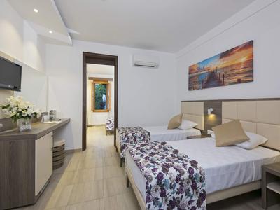 Modernes Hotelzimmer mit zwei Einzelbetten, floralem Bettüberwurf und hellem Holzmöbel.