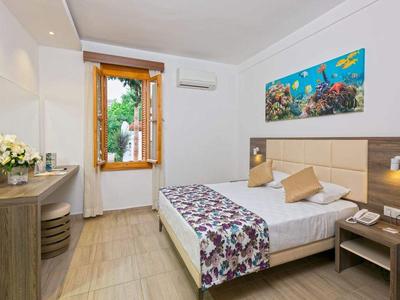 Helles Schlafzimmer mit großem Bett, Holzfenster, Schreibtisch, Stuhl und farbenfrohem Meeresbild.