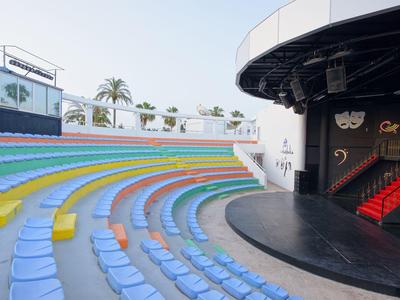 Bunte Sitzreihen eines halbkreisförmigen Amphitheaters mit kleiner Bühne und Treppen links.