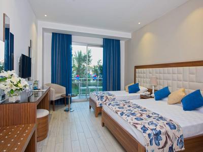 Modernes Hotelzimmer mit Doppelbett, blauen Vorhängen und Balkon mit Blick ins Grüne.
