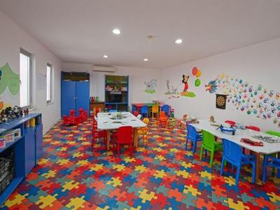 Hell gestalteter Spielraum mit buntem Puzzlemattenboden, kindgerechten Tischen, Stühlen und Wandbildern.