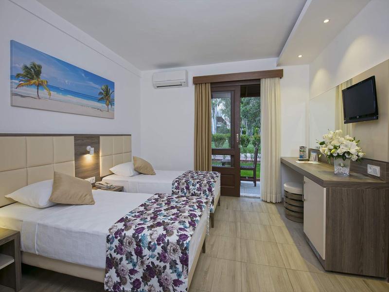 Habitación de hotel moderna con dos camas individuales, TV y acceso a un jardín.