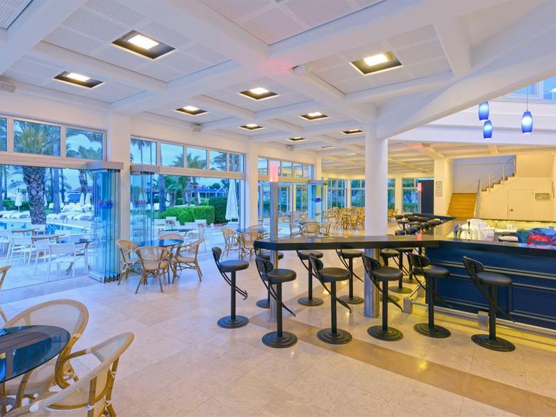 Área de comedor luminosa con taburetes altos, mesas y grandes ventanas con vista a un espacio al aire libre.