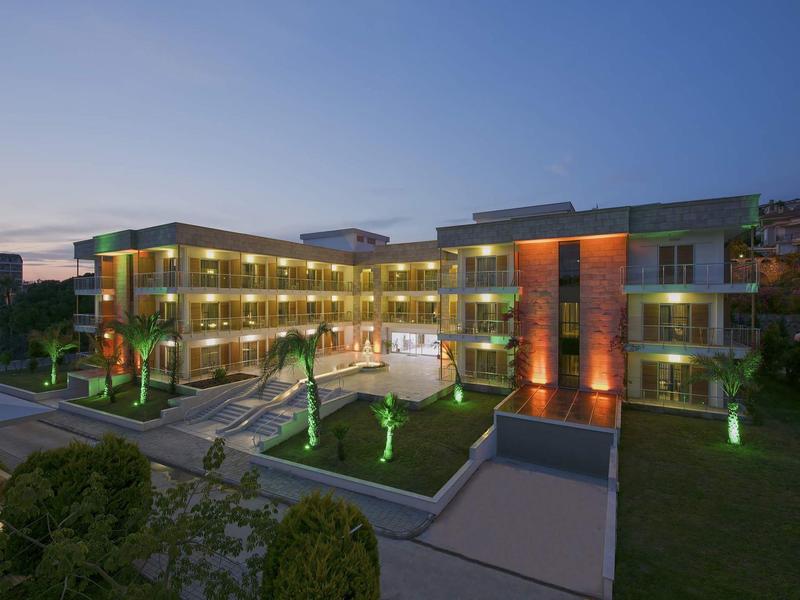 Edificio de hotel moderno al atardecer con fachada iluminada y jardín.