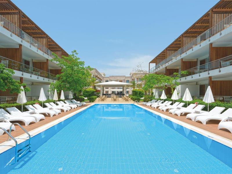 Gran piscina al aire libre entre edificios de hotel de dos pisos con tumbonas y sombrillas.