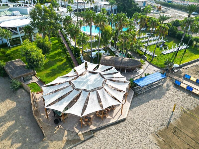 Bar en la playa con sombrillas y palmeras, rodeado de piscina y tumbonas del hotel.