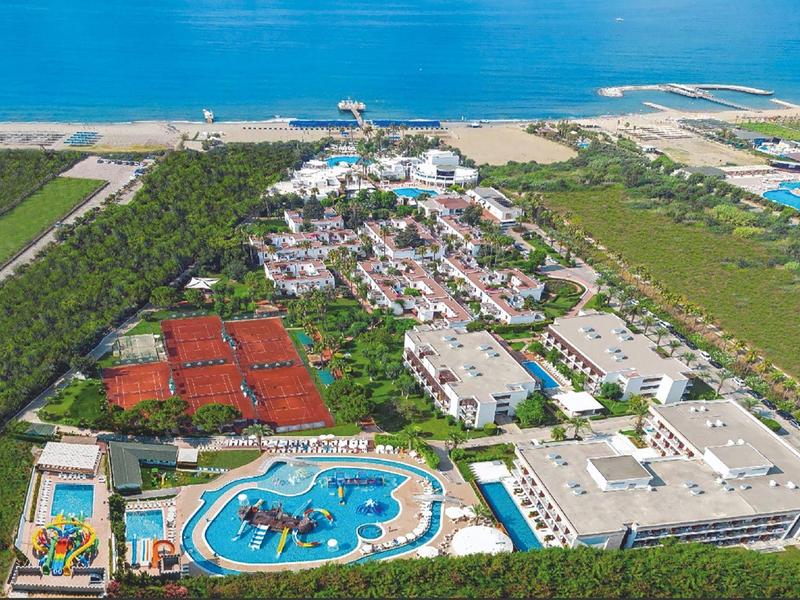 Vista aérea de un resort con piscina, canchas de tenis y playa junto al mar.