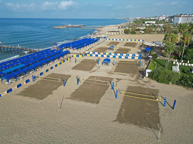 Una amplia playa arenosa con tiendas de playa azules y redes de voleibol bajo un cielo despejado.