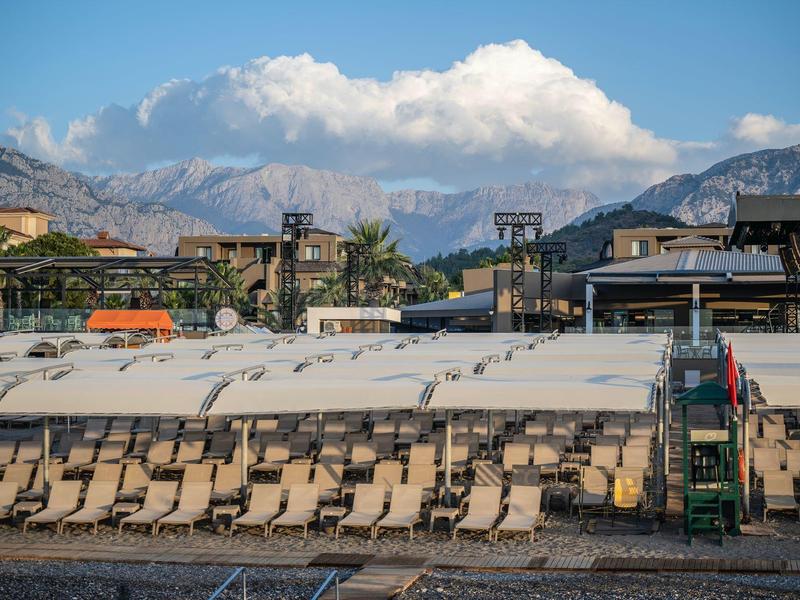 Fila de tumbonas vacías frente a una piscina con montañas y cielo azul al fondo.