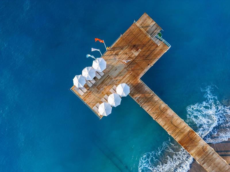 Muelle de madera con sombrillas blancas sobre agua clara y azul, vista aérea.