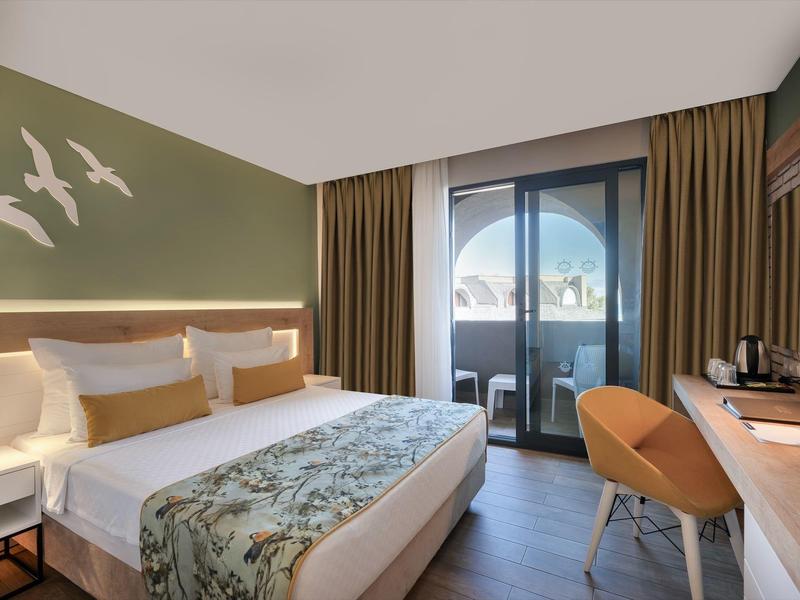 Habitación de hotel moderna con cama doble, balcón y decoración elegante en tonos cálidos.