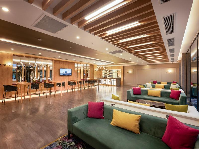 Amplia sala de estar de hotel elegantemente decorada con sofás coloridos y barra moderna al fondo.