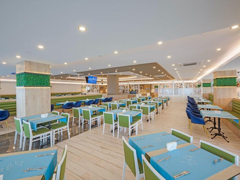 Comedor moderno con sillas azules y verdes, muebles de madera clara y luces en el techo.