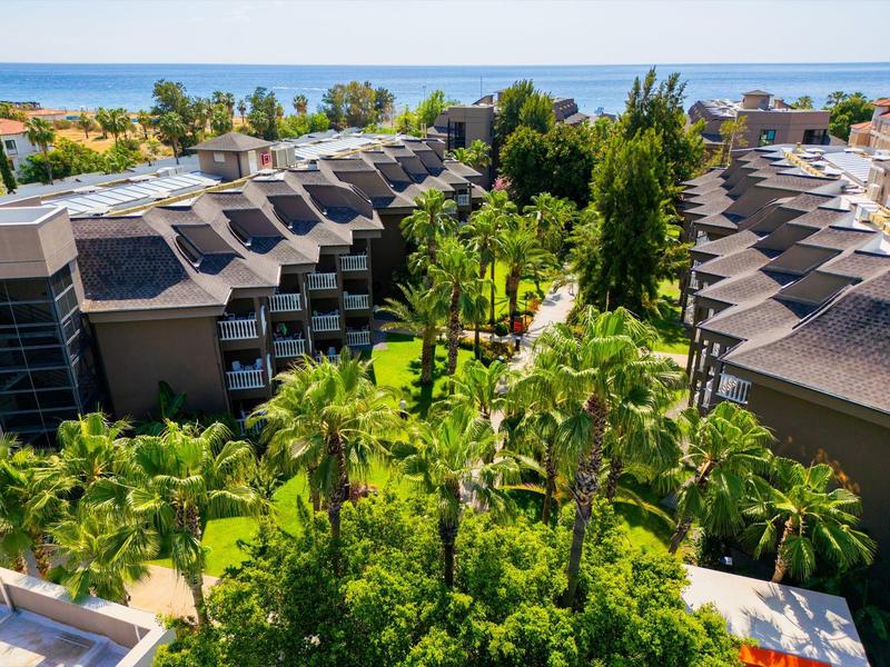 Vista de un resort con dos edificios, jardines tropicales y el mar al fondo.