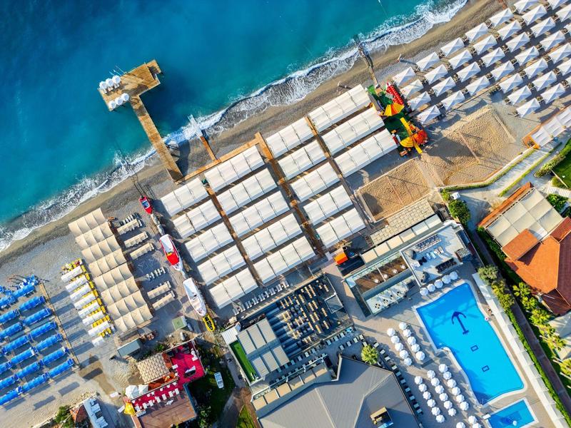 Vista aérea de una playa con tumbonas, piscina y muelle en el mar.