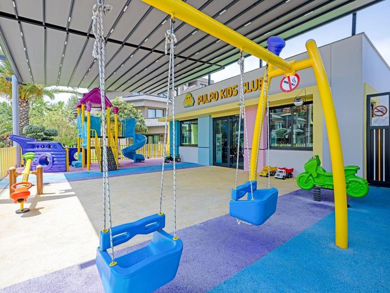 Área de juegos al aire libre con columpios y estructura para escalar en un hotel.