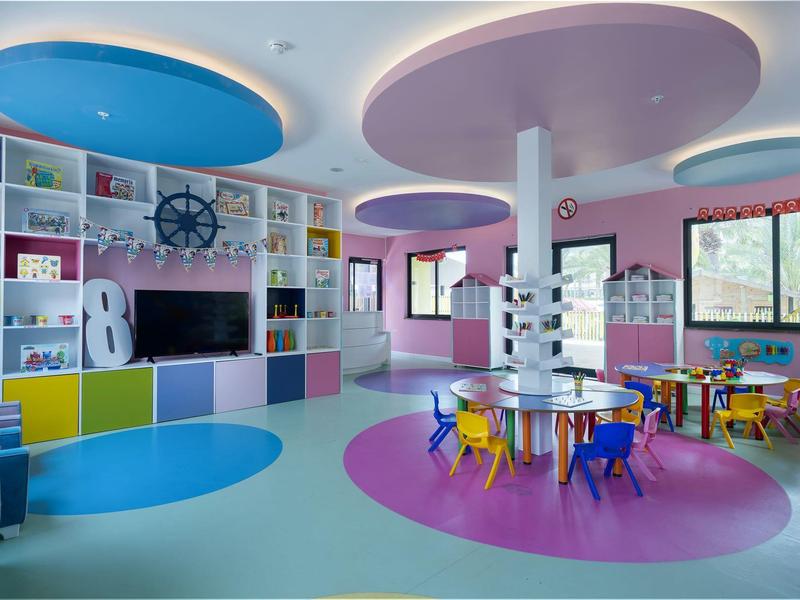 Sala de juegos infantil colorida con grupos de asientos y pared de estantes bien equipada.