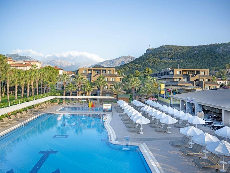 Área de piscina de hotel moderno con tumbonas, sombrillas y vista a la montaña.