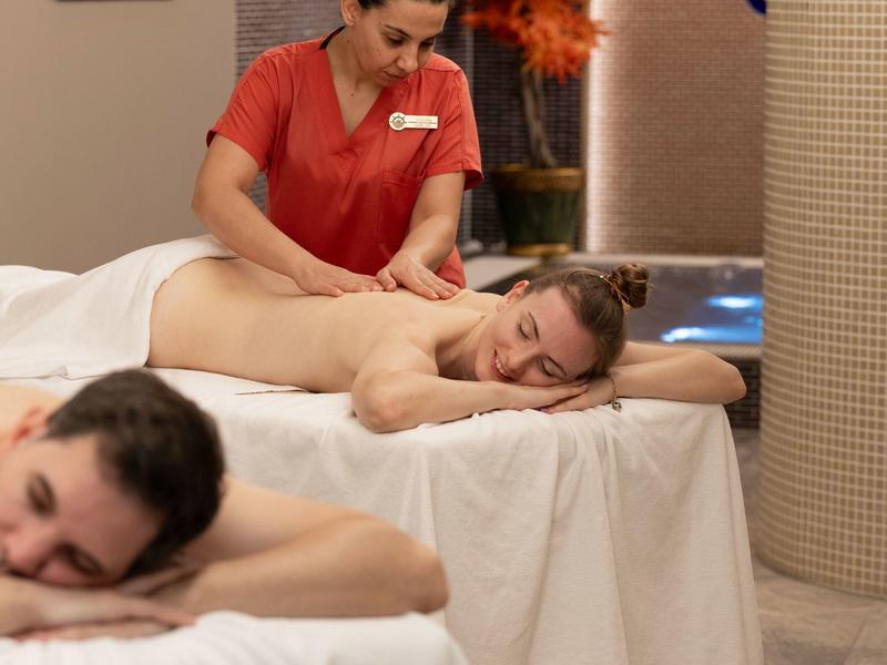 Dos personas se relajan juntas recibiendo un masaje en un área de spa.