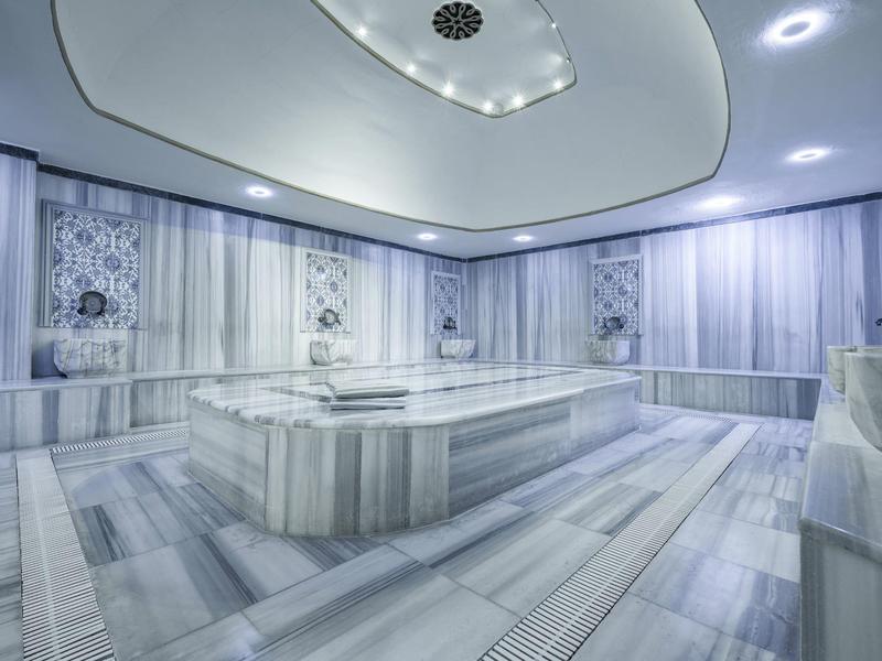 Hamam turco moderno y elegante con mármol claro y plataforma central calefaccionada.