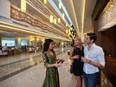 Drei Menschen im Hotel lobby, zwei trinken und eine hält ein Buch, helle und elegante Umgebung.