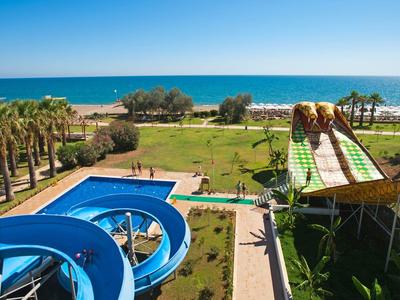 Wasserpark mit blauen Rutschen, Palmen und Blick aufs blaue Meer bei sonnigem Himmel.