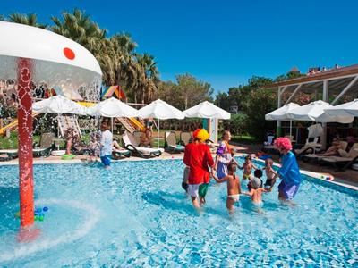 Kinder spielen im flachen Pool mit Wasserspielen und Sonnenschirmen bei klarem Himmel.