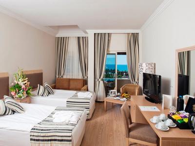 Helles Hotelzimmer mit Doppelbett, Schreibtisch, Fernseher, Sitzbereich und Meerblickfenster.