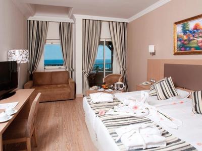 Gemütliches Hotelzimmer mit Doppelbett, Sofa, Fernseher und Balkon mit Meerblick.