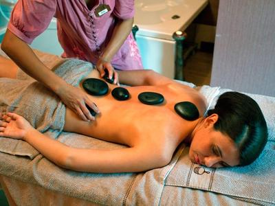 Frau liegt entspannt auf Massagetisch mit warmen, schwarzen Hot-Stone-Steinen auf Rücken.