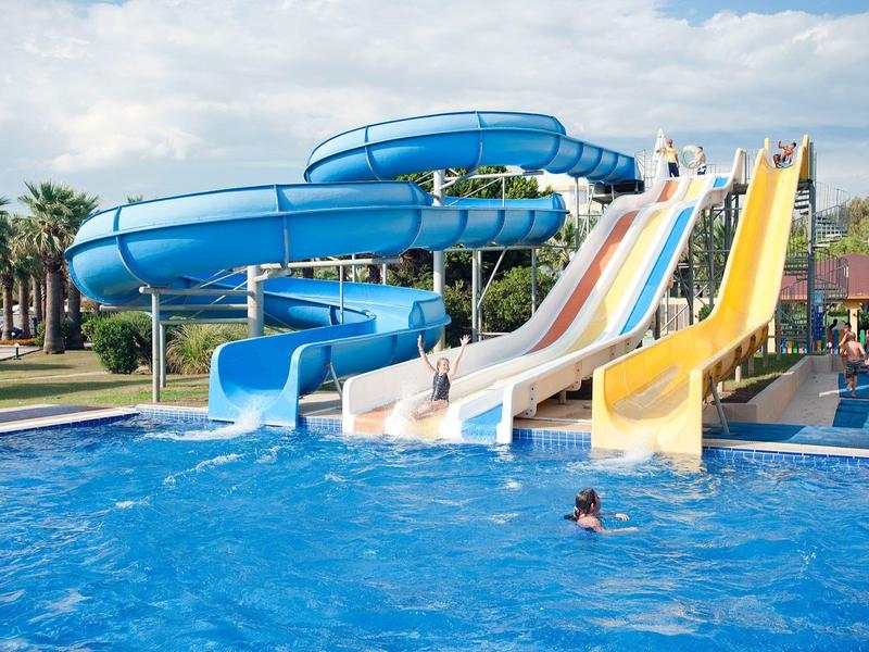 Several colorful water slides lead into a large pool with people.