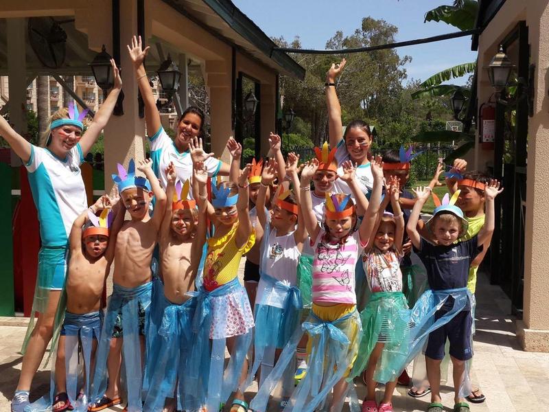 Group of joyful children celebrating with colorful costumes and raised arms in sunny outdoor area.