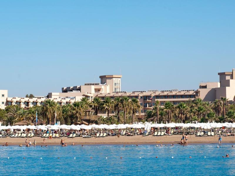 Beach with many umbrellas and hotel buildings in the background by the sea.