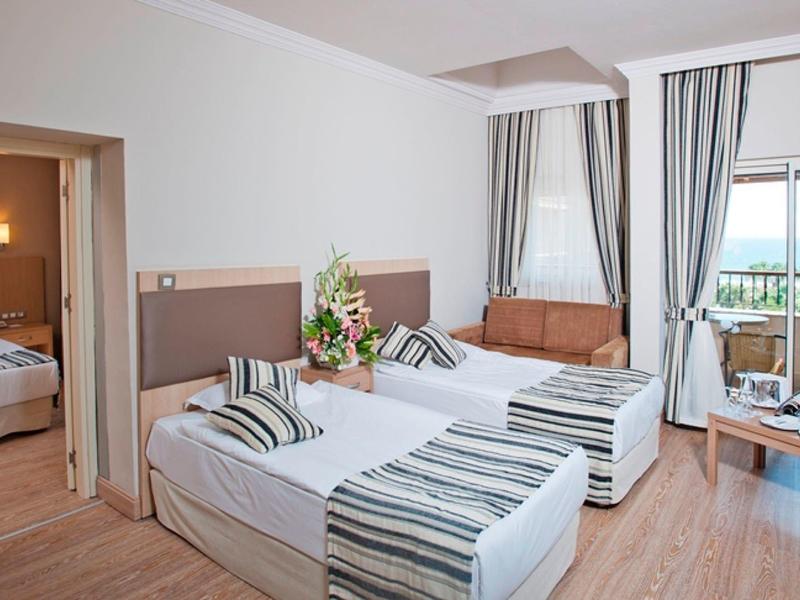 Bright hotel room with two single beds, balcony access, and sea view.