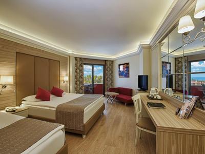 Jasně zařízený hotelový pokoj se dvěma postelemi, psacím stolem a balkónem s výhledem na moře.