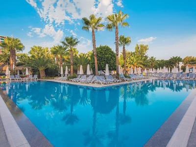 Großer Pool mit Liegestühlen und Palmen in einem Hotelresort unter blauem Himmel