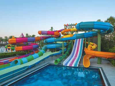 Bunte Wasserrutschen in einem Freizeitpark neben einem Pool unter klarem Himmel.