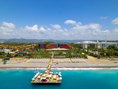 Hotelový komplex s písečnou pláží, lehátky a molu s posezením nad mořem.