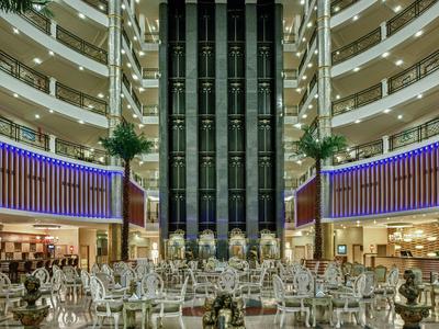 Moderní hotelová lobby s centrálními skleněnými výtahy, odpočinkovou zónou a průchozími patry.