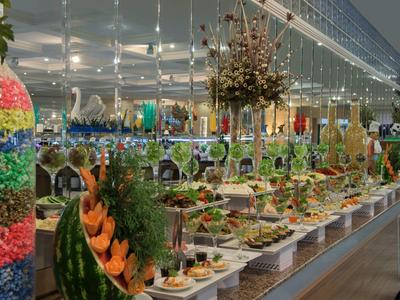 Dlouhý bufetový stůl s různými pokrmy a květinovými aranžmá v slavnostně vyzdobeném prostoru.