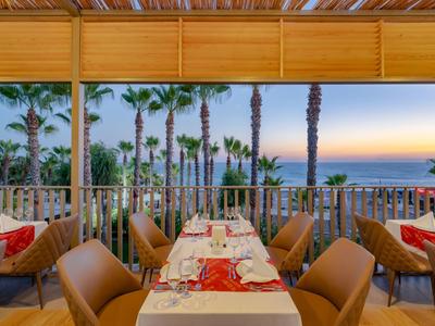 Terasa s prostřenými stoly s výhledem na palmy a moře při západu slunce.