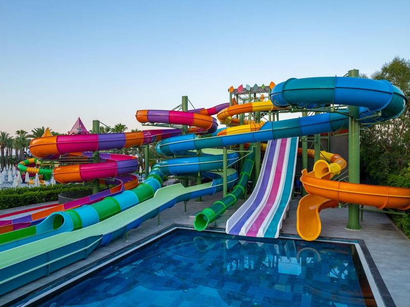 Barevné vodní skluzavky vedou do čistého bazénu pod slunečnou oblohou v zábavním parku.