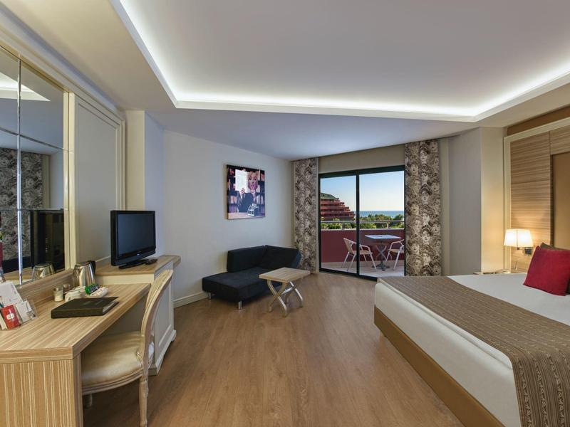Moderně zařízený hotelový pokoj s manželskou postelí, psacím stolem a balkonem s výhledem.