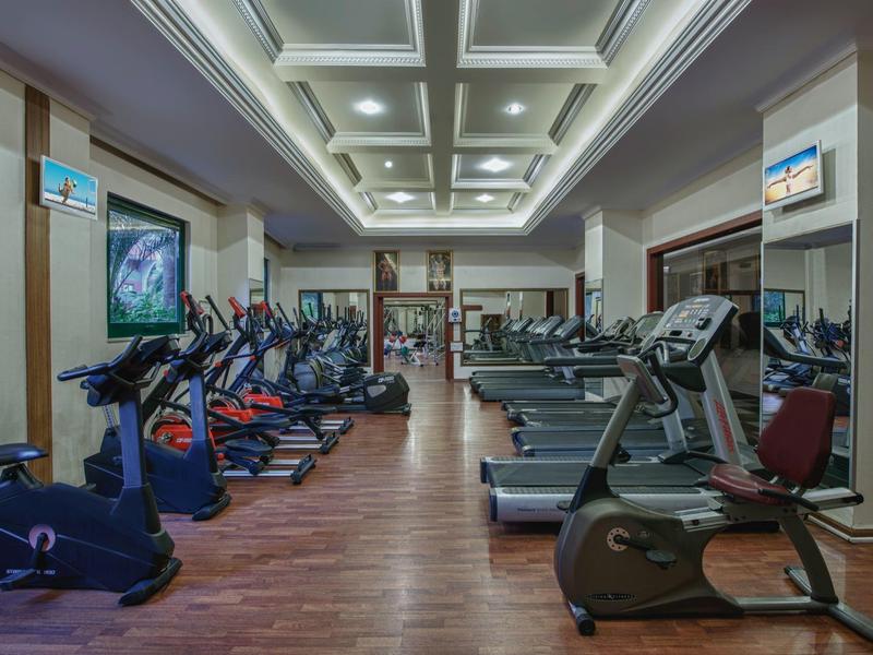 Moderní fitness místnost s různými kardio stroji a dřevěnou podlahou v hotelu.