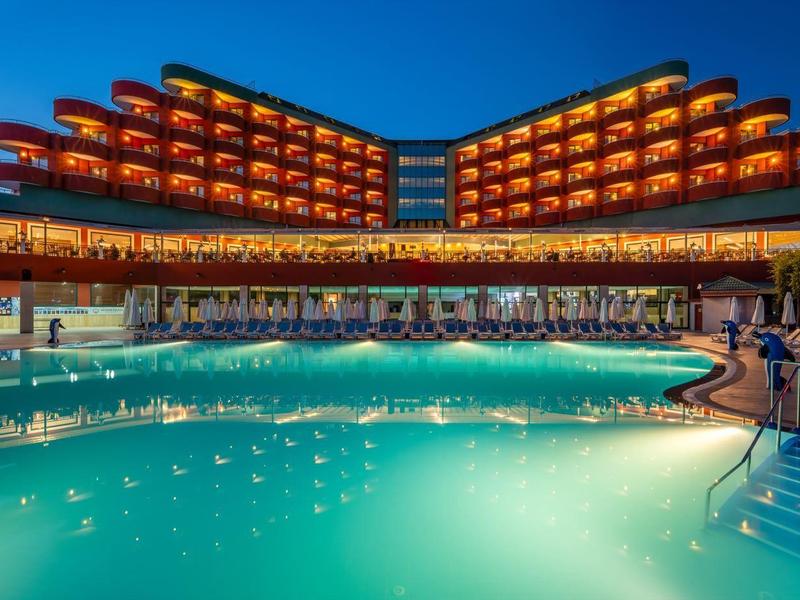 Moderní hotel s osvětleným bazénem a lehátky v nočním prostředí.