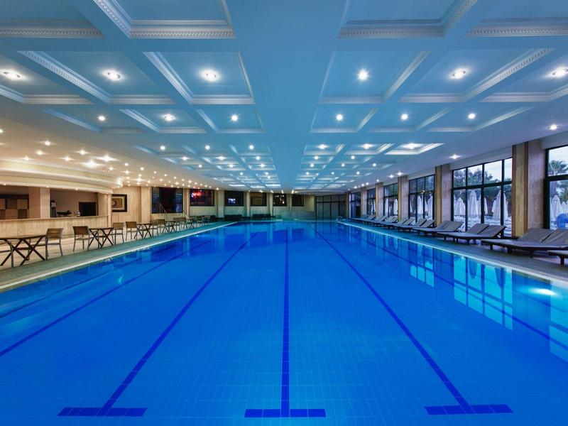 Velký krytý bazén s modrými dlaždicemi, posezením a velkými okny