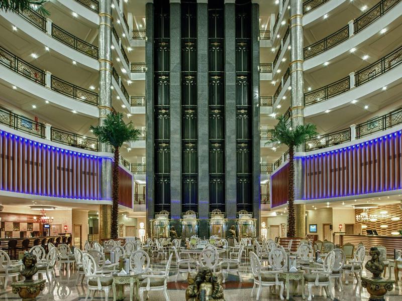 Moderní hotelová lobby s centrálními skleněnými výtahy, odpočinkovou zónou a průchozími patry.