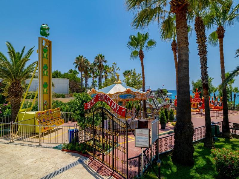 Slunná hotelová zahrada s palmami, květinami a výhledem na moře za jasného dne.