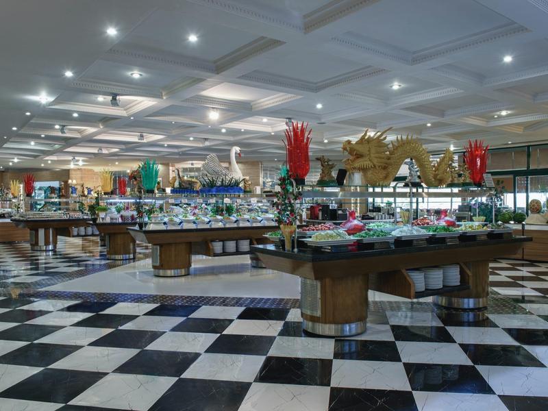 Velká bufetová oblast s kulatými stoly zdobenými květinami a mnoha pokrmy.